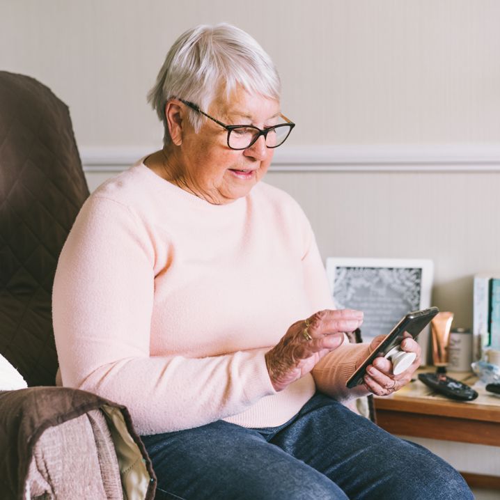 Äldre kvinna med glasögon och rosa tröja sitter och tittar på sin telefon