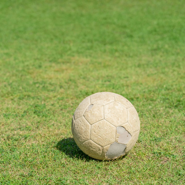 En gammal, använd och sliten, vit fotboll ligger på gräset