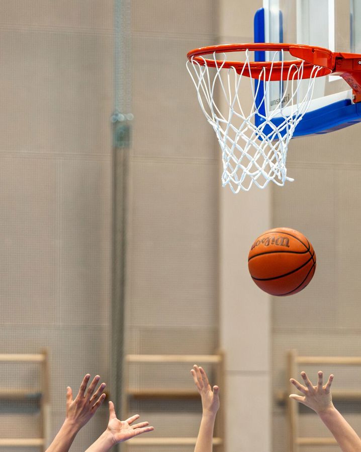 Barnhänder som sträcker sig efter basketboll som faller genom basketkorgen