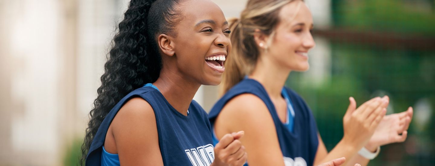 Två sportklädda tjejer klappar händerna och hejar
