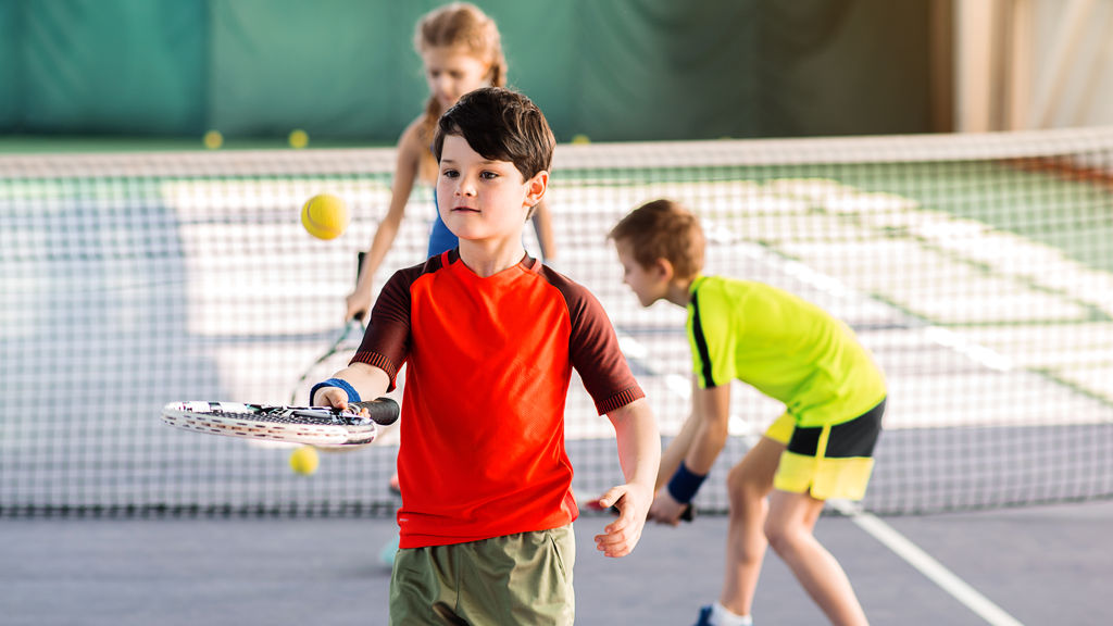 tre barn på en tennisbana som bollar med racket och boll