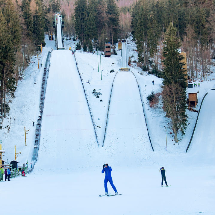 Två personer på skidor som skidar nedanför en backhoppningsbacke