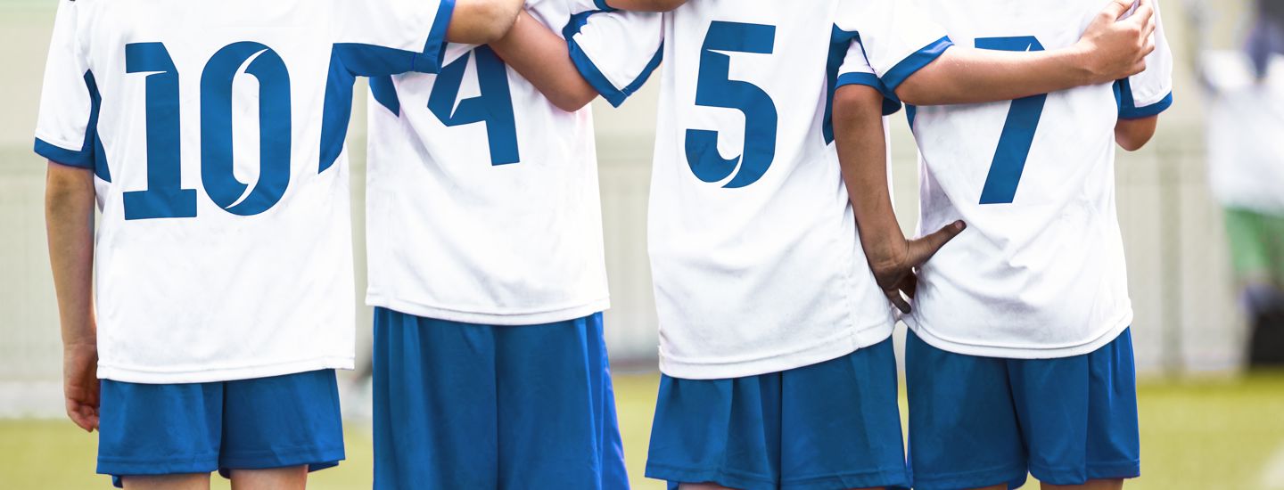 Matchklädda barn håller armarna om varandra på en gräsplan med en fotboll liggandes bredvid