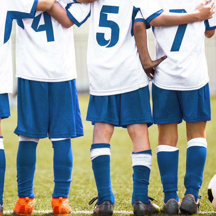Matchklädda barn håller armarna om varandra på en gräsplan med en fotboll liggandes bredvid
