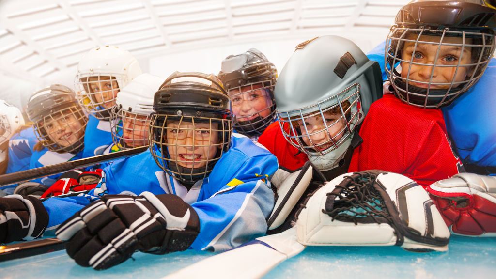 Barn med ishockeyutrustning ligger på mage på isen