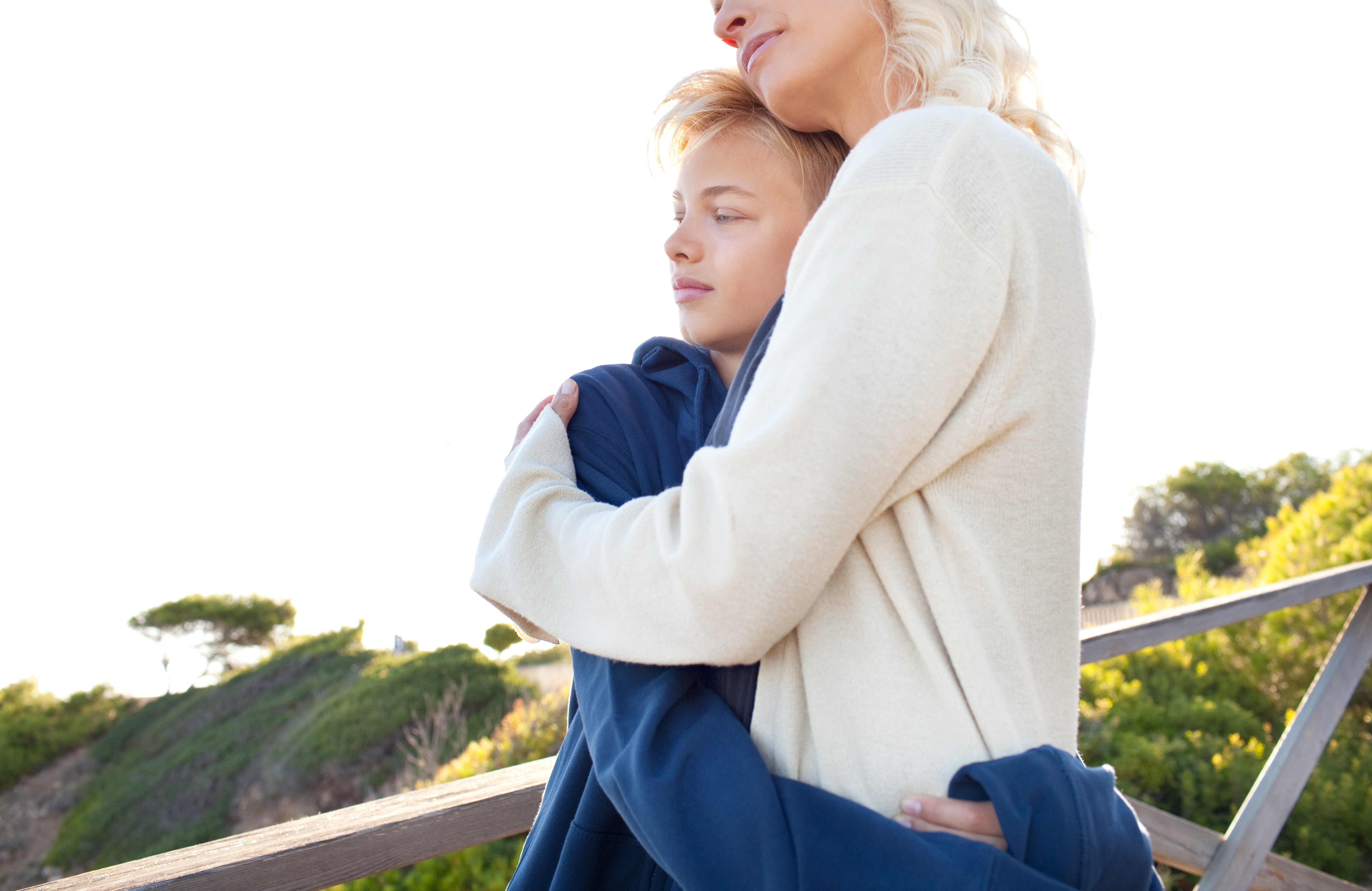 En mamma och son som kramas i en grönskande utomhusmiljö