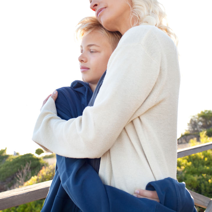 En mamma och son som kramas i en grönskande utomhusmiljö