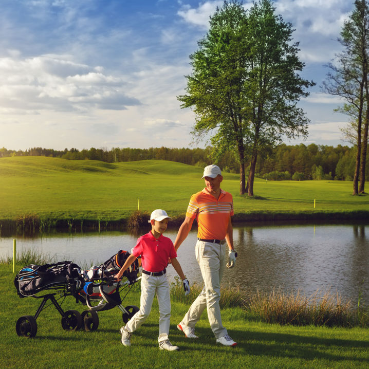 En man och en pojke drar varsina golfvagnar på en golfbana vid ett vattendrag