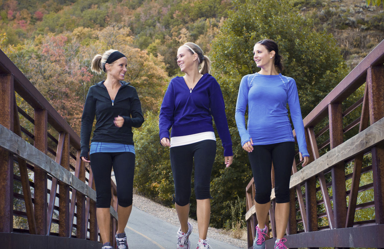 Tre kvinnor som powerwalkar utomhus och går över en bro