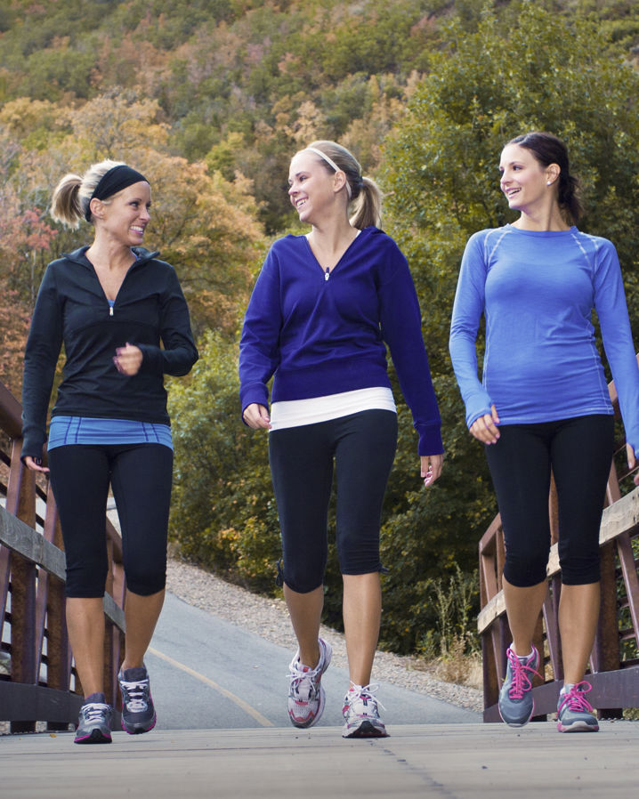 Tre kvinnor som powerwalkar utomhus och går över en bro
