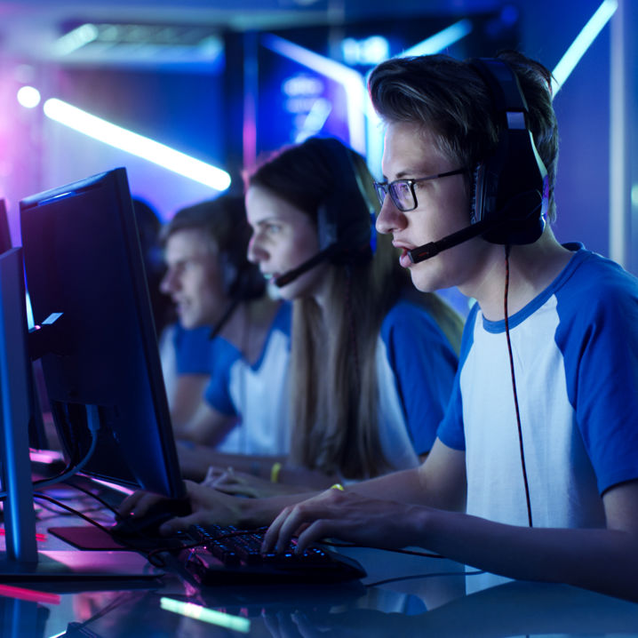 Ett e-sportlag sitter bredvid varandra med datorskärmar framför sig. Rummet har industriell och neonfärgad dekor.