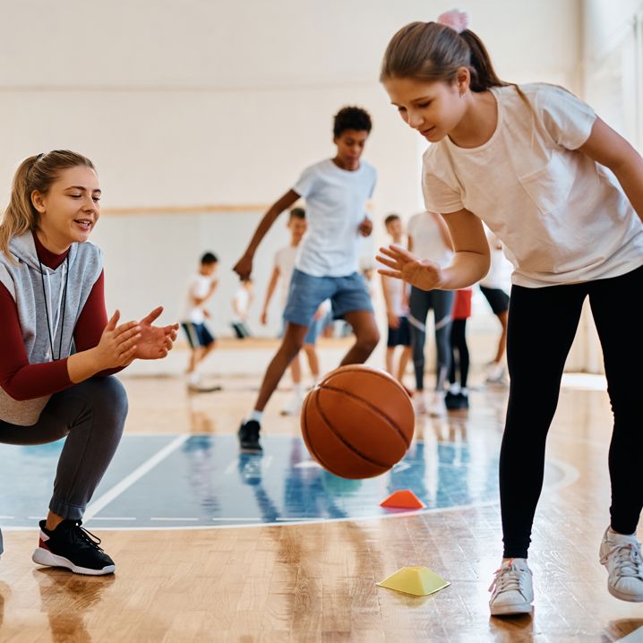 Ungdomar som tränar basket inomhus, en tränare sitter på knä och klappar händerna
