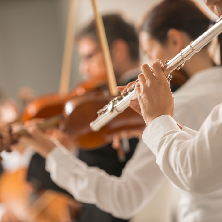 En inzoomad bild på en orkester där tre personer spelar fiol och flöjt