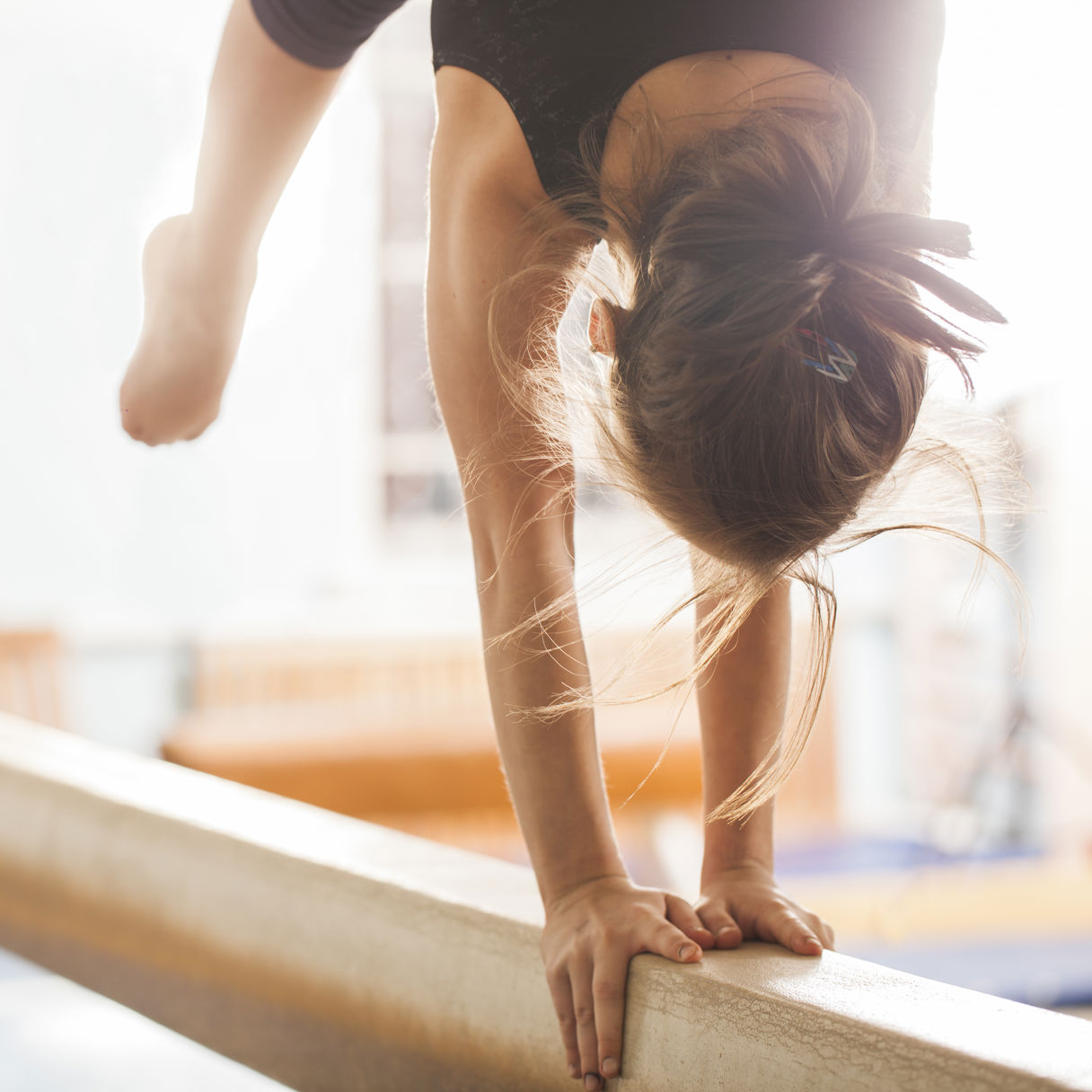 Flicka som tränar gymnastik handstående på en bom