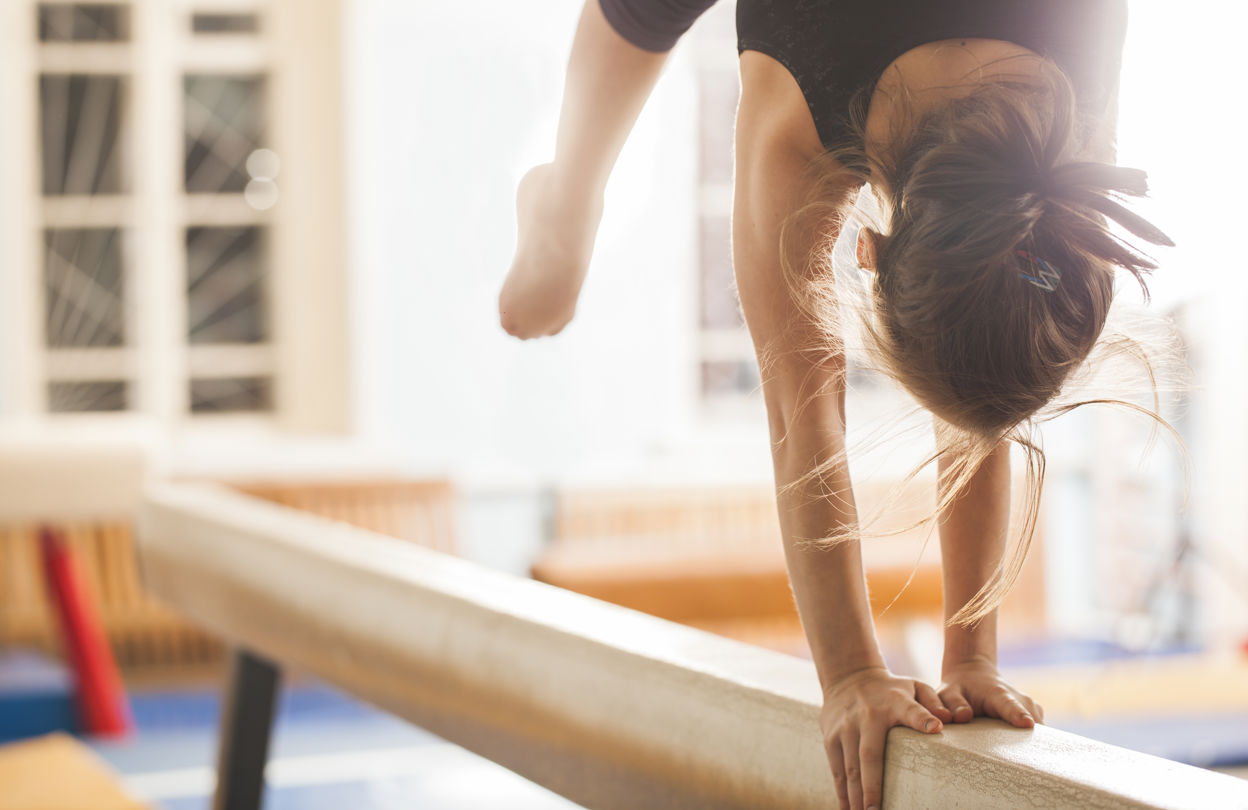 Flicka som tränar gymnastik handstående på en bom