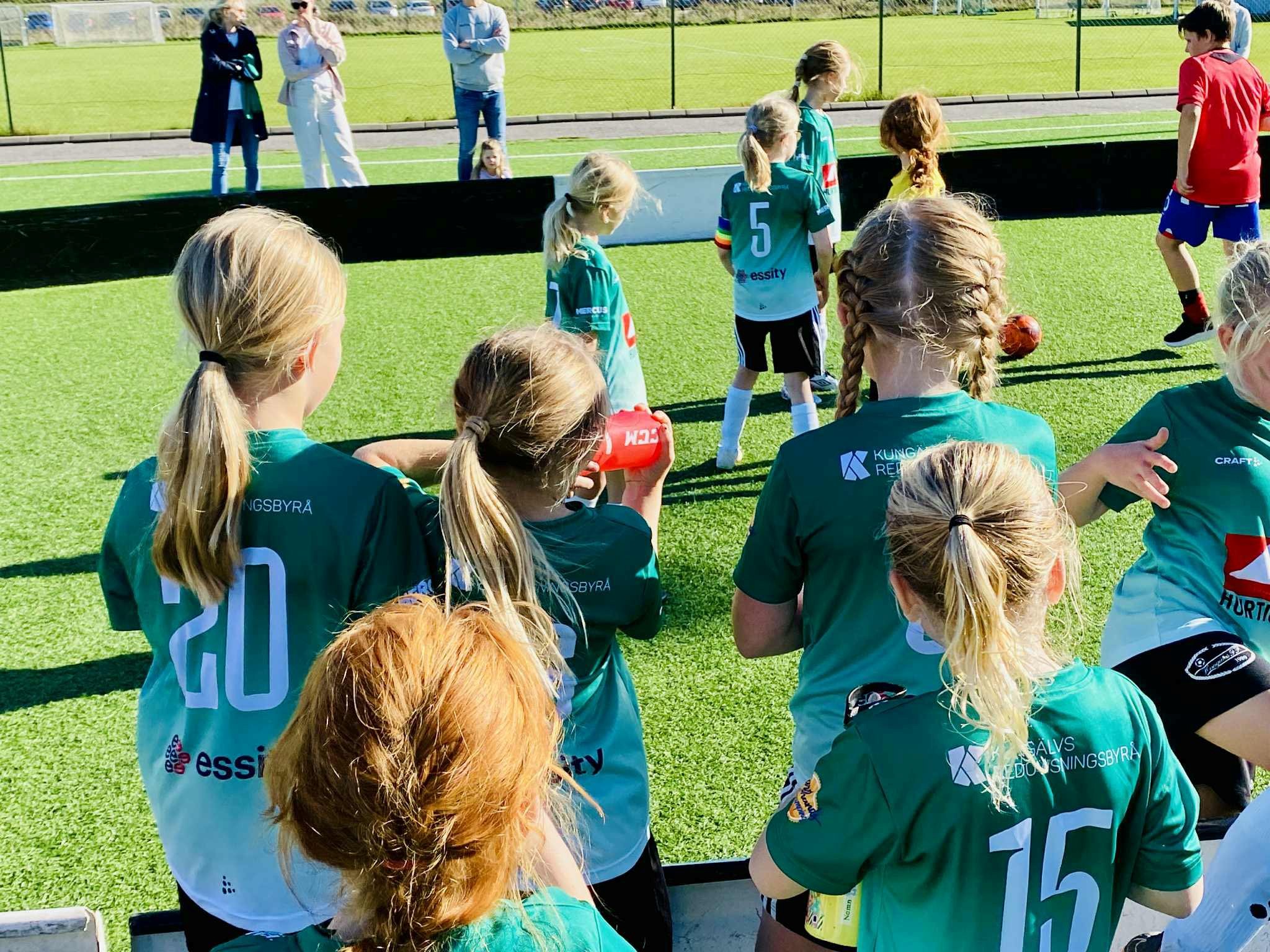 flickor i gröna fotbollströjor spelar fotboll på fotbollsplan