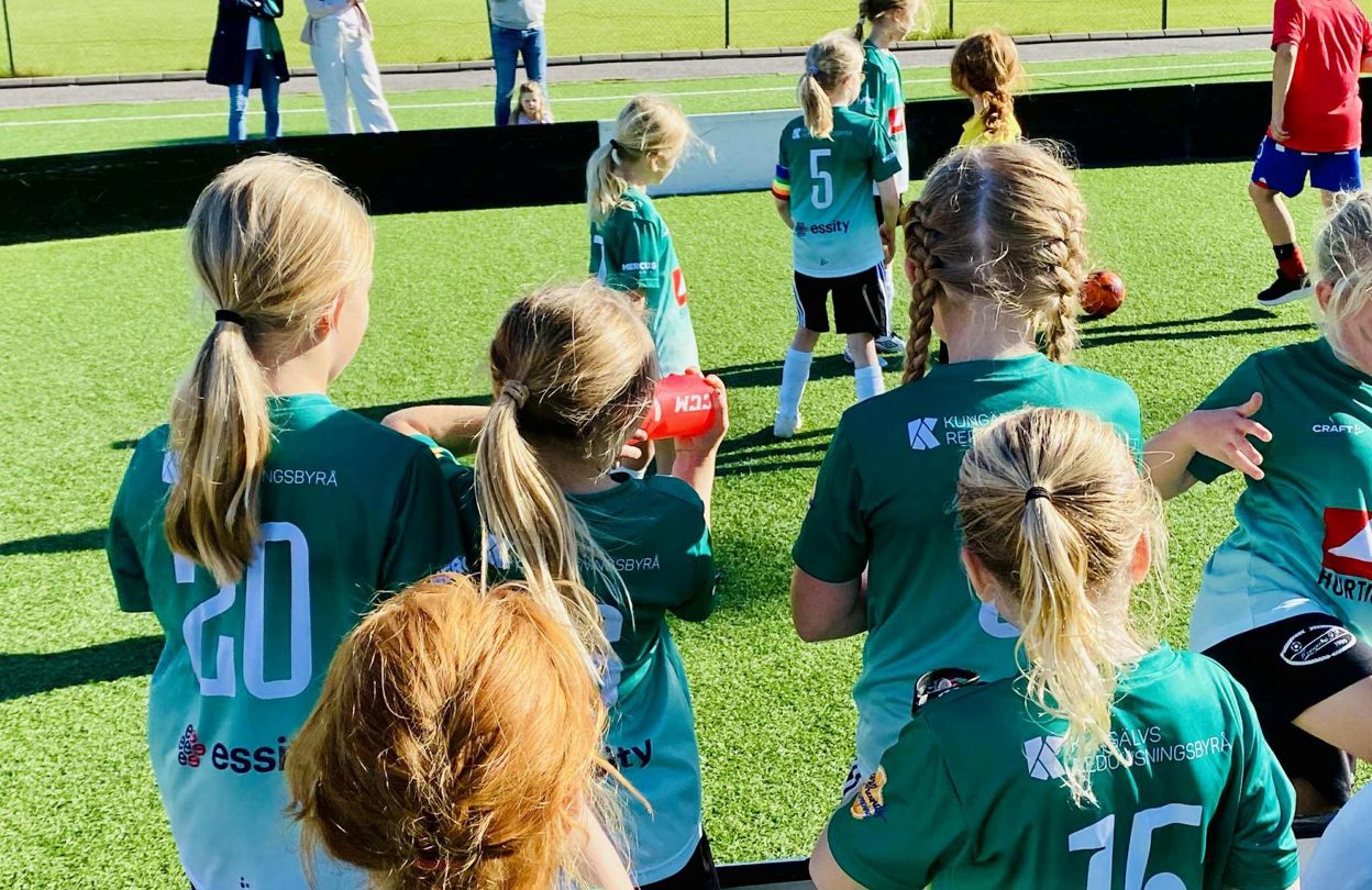 flickor i gröna fotbollströjor spelar fotboll på fotbollsplan