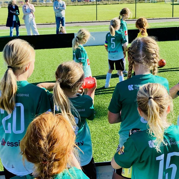 flickor i gröna fotbollströjor spelar fotboll på fotbollsplan