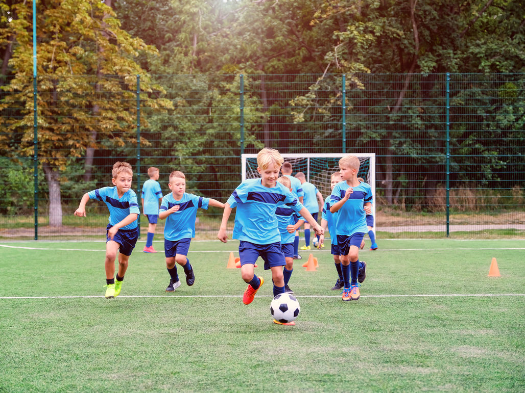 En pojke driver en fotboll på en fotbollsplan, med flera lagkamrater springande bakom honom