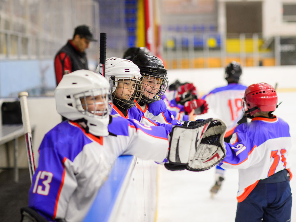 Barn i hockeyutrustning, några åkandes på isen, och några som står i avbytarbåset.