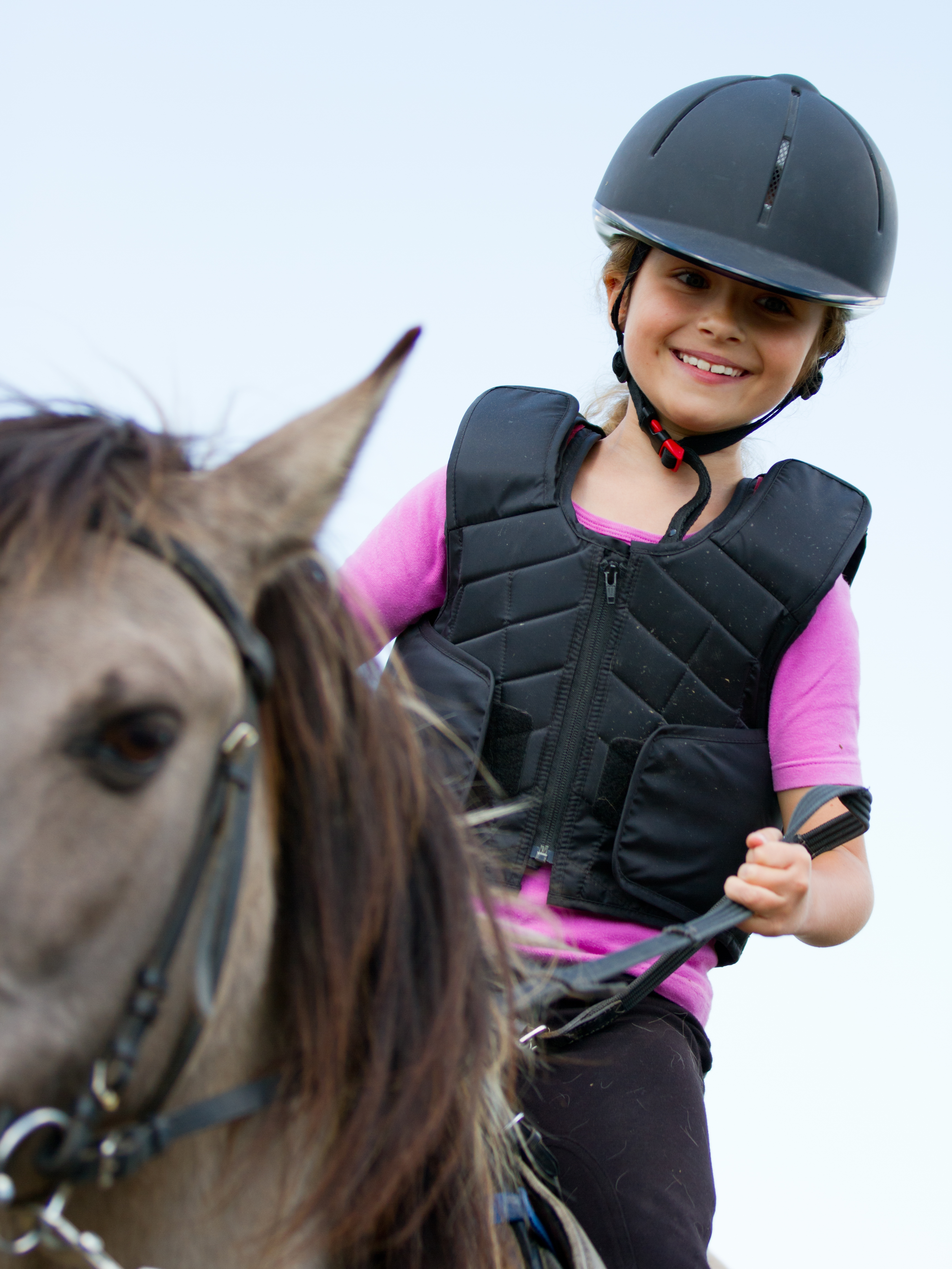 En leende flicka i ridhjälm, och ridväst rider på en häst