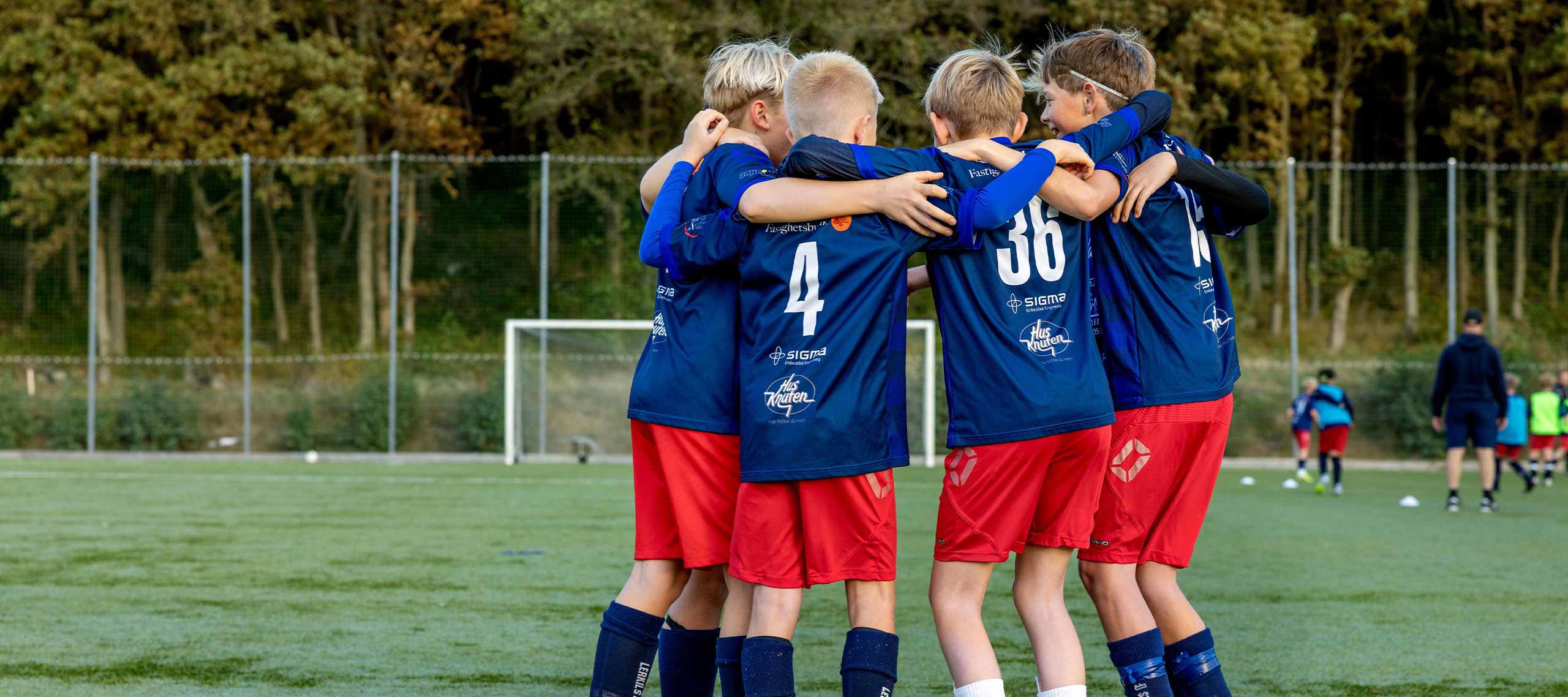 Pojkar i fotbollskläder firar i en ring och håller varandra om axlarna