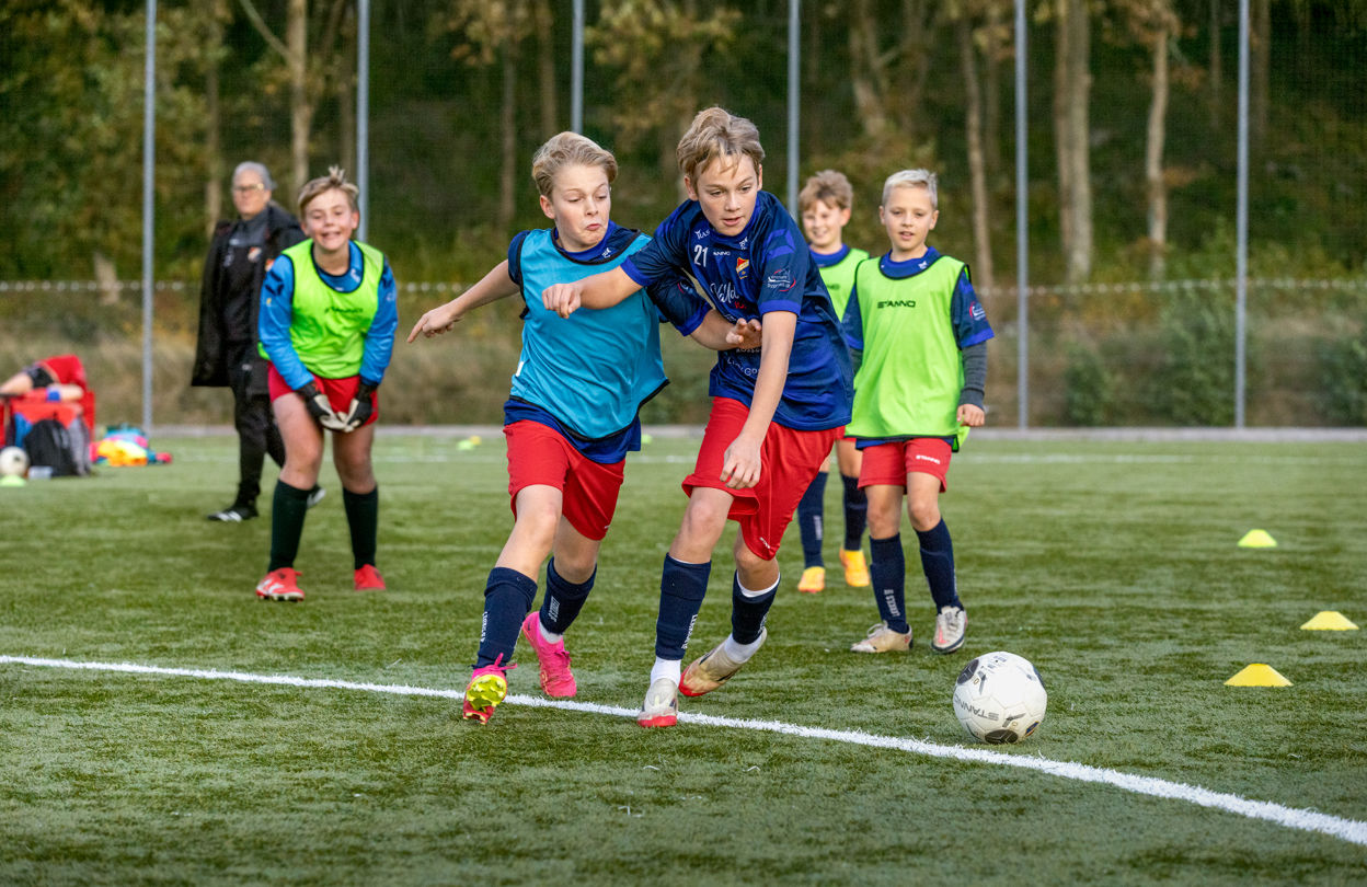 Pojkar som spelar fotboll, varav två av dem i intensiv närkamp om bollen