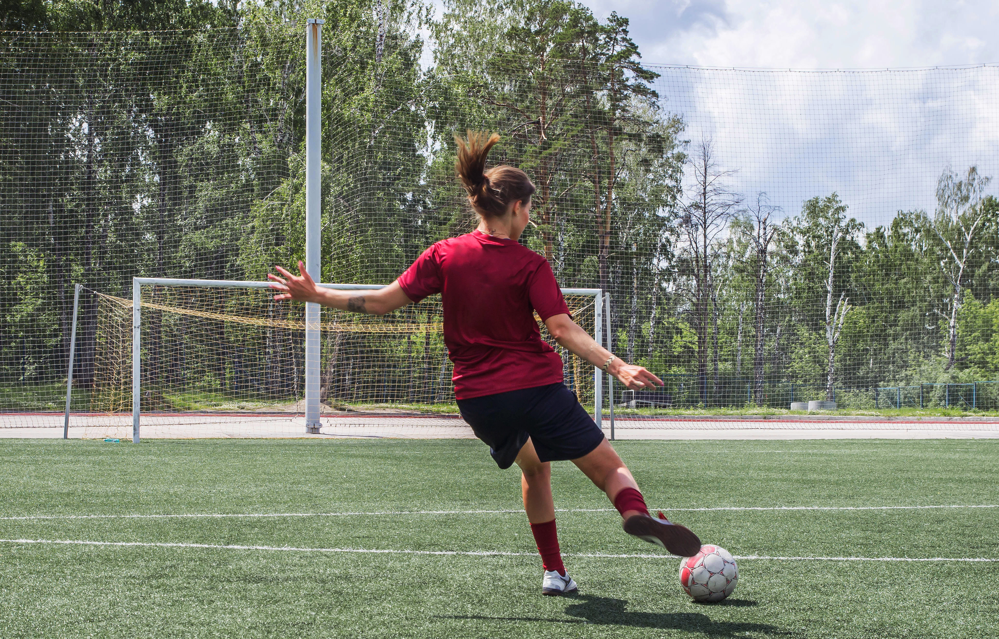 Fotbollsklädd tjej skjuter mot ett fotbollsmål på en gräsplan