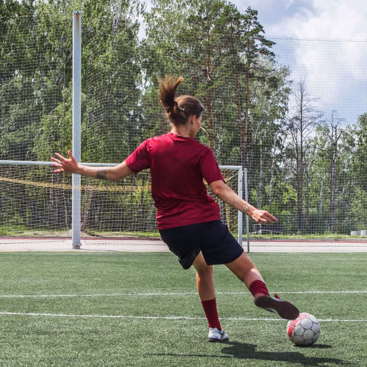 Fotbollsklädd tjej skjuter mot ett fotbollsmål på en gräsplan