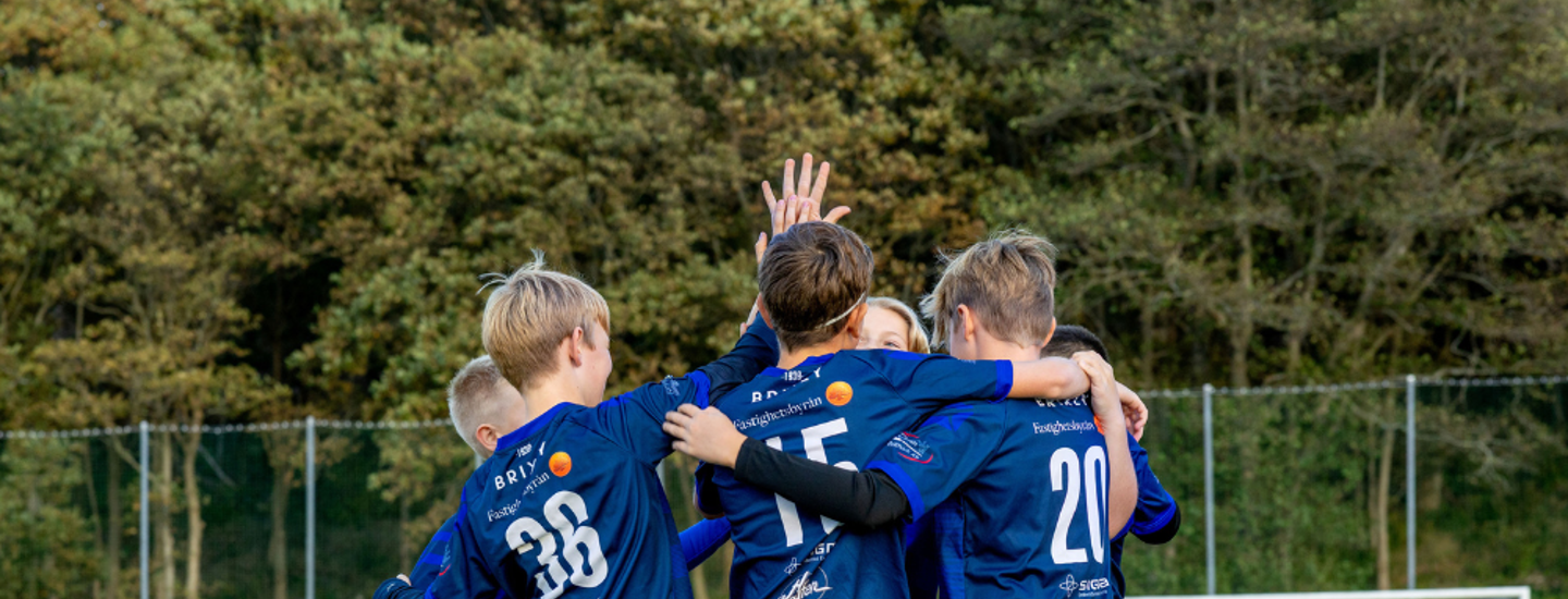 Pojkfotbollslag står på planen, kramas och gör high five