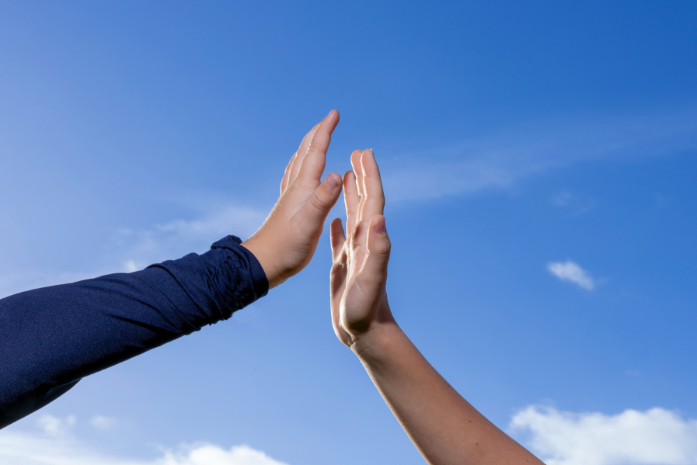 Två händer möts för en high five mot en klarblå himmel