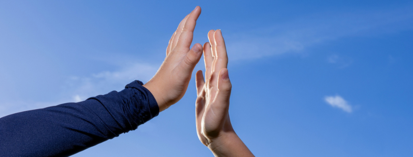 Två händer möts för en high five mot en klarblå himmel