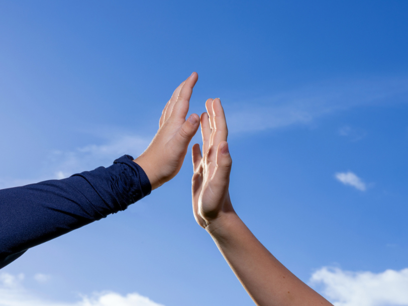 Två händer möts för en high five mot en klarblå himmel
