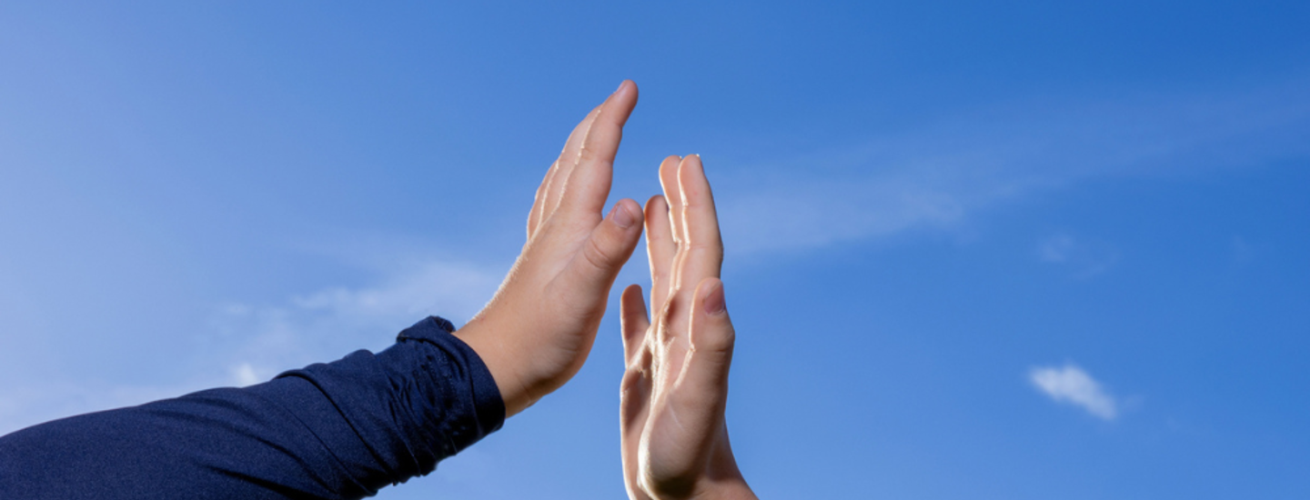 Två händer möts för en high five mot en klarblå himmel