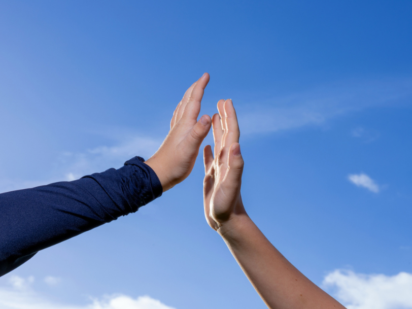 Två händer möts för en high five mot en klarblå himmel