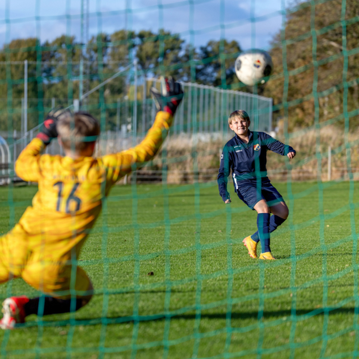 Målvakt i gult matchset slänger sig och försöker rädda ett skott