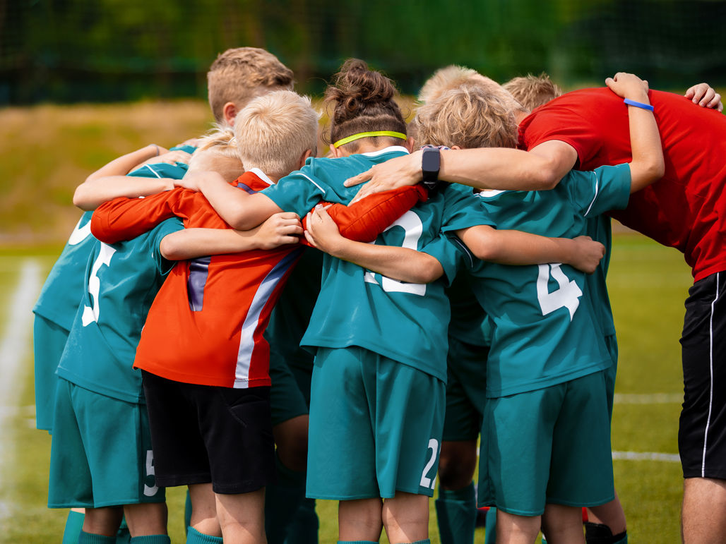 Ett ungt pojklag i matchkläder står i en ring med armarna om varandra på en fotbollsplan