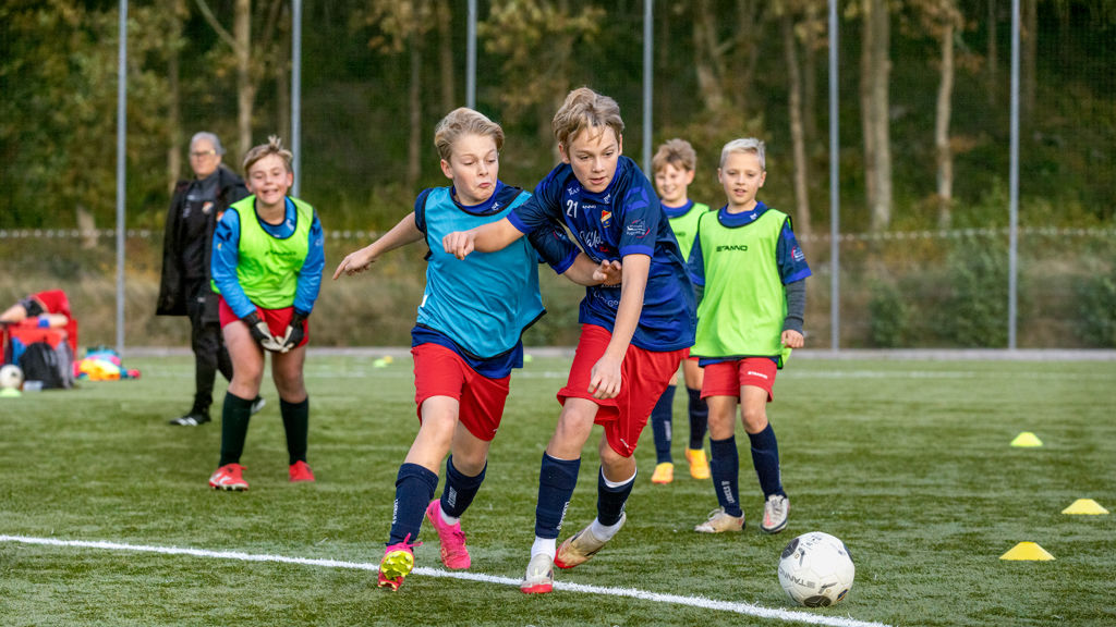 Pojkar som spelar fotboll, varav två av dem i intensiv närkamp om bollen