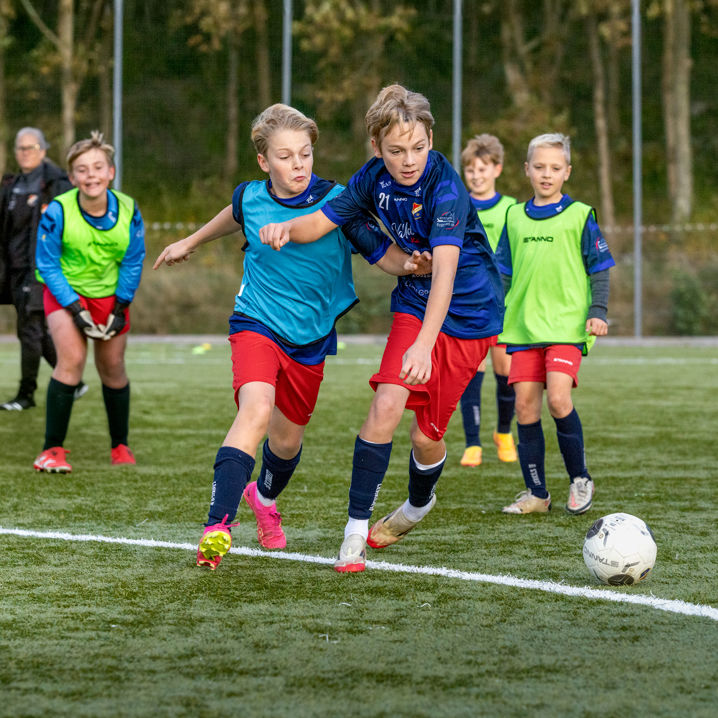 Pojkar som spelar fotboll, varav två av dem i intensiv närkamp om bollen