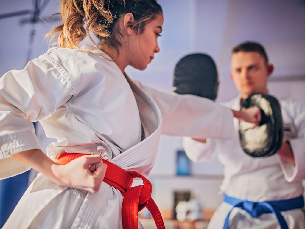 Flicka i kampsportskläder tränar slag mot en man som håller upp mitsar