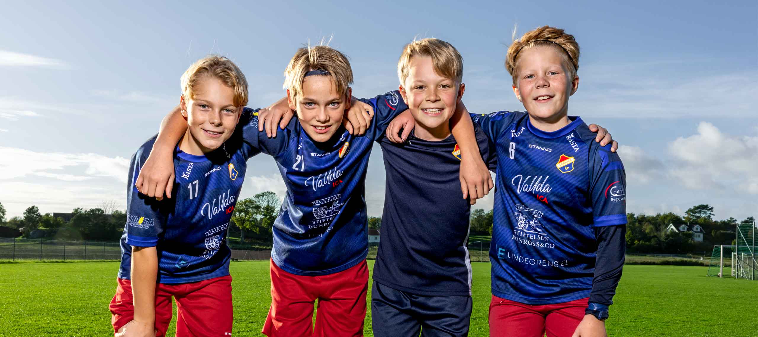 Fyra pojkar på en fotbollsplan som ler och håller om varandra