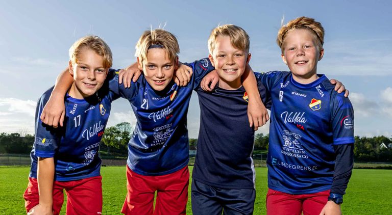 Fyra pojkar på en fotbollsplan som ler och håller om varandra