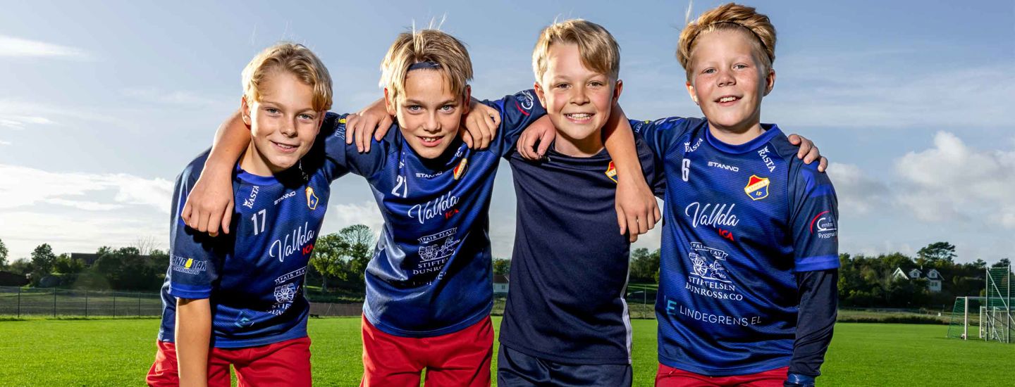 Fyra pojkar på en fotbollsplan som ler och håller om varandra