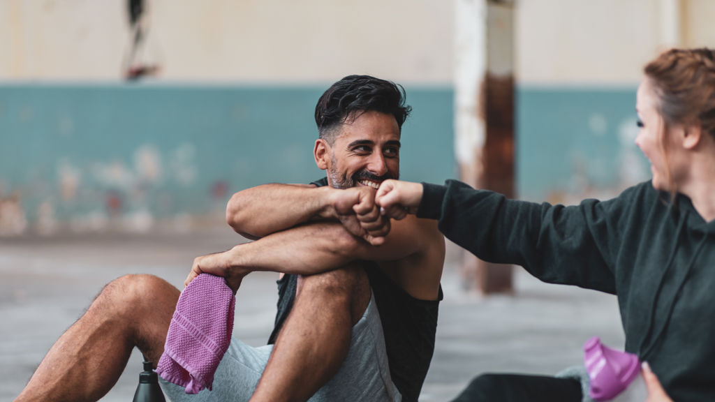 En man och en kvinna sitter på ett golv i en träningslokal och fistbumpar varandra