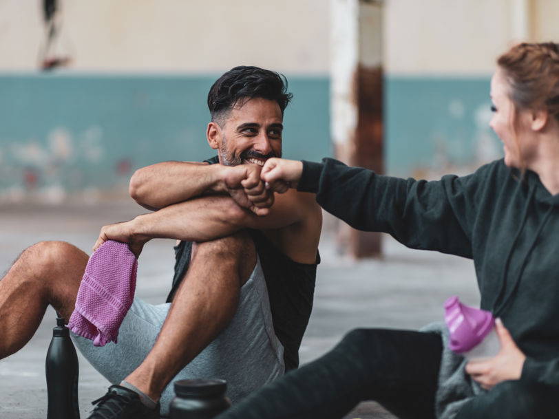 En man och en kvinna sitter på ett golv i en träningslokal och fistbumpar varandra