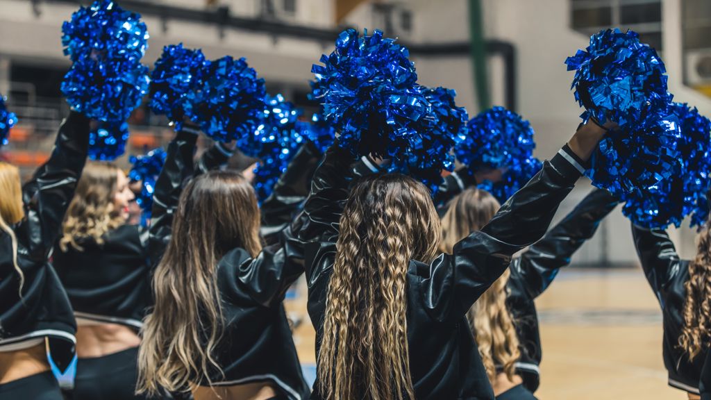 Cheerleaders som lyfter sina blå pompoms över huvudet