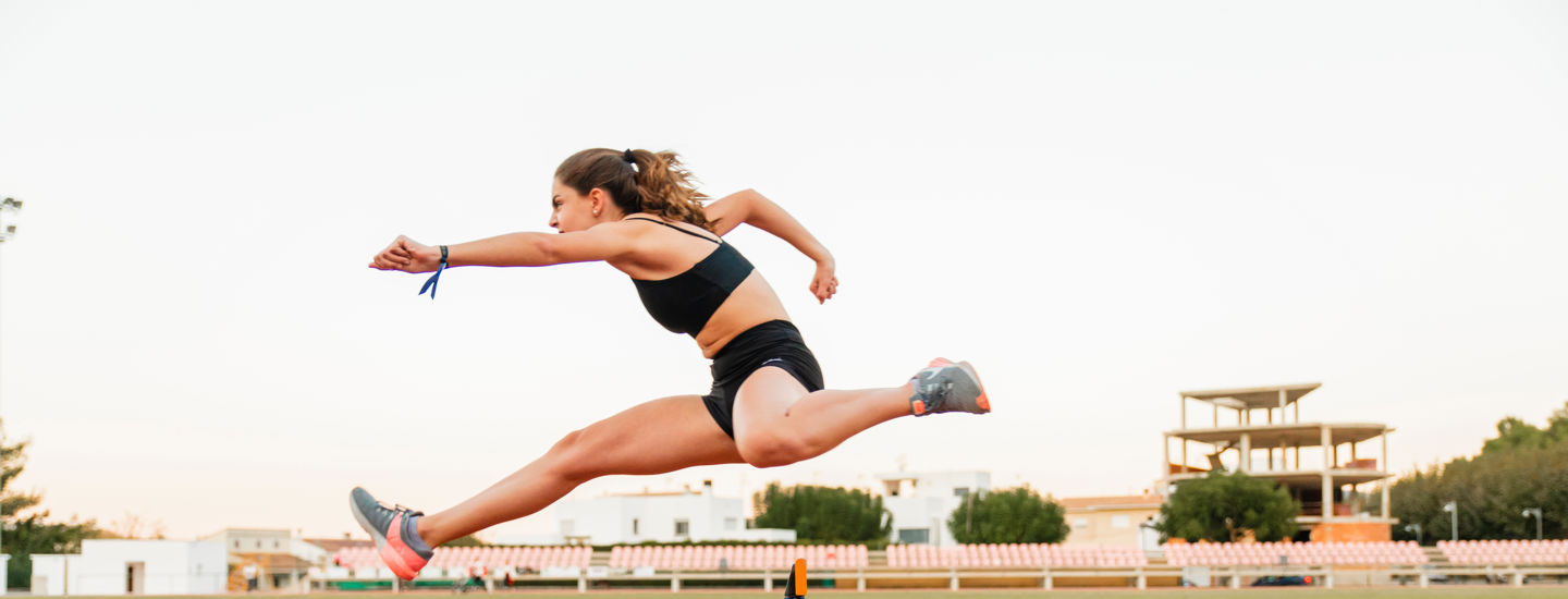 Kvinna som hoppar över en häck på en friidrottsbana