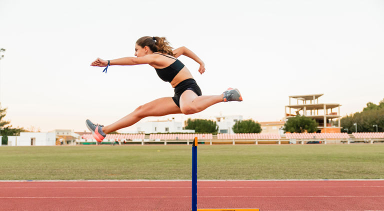 Kvinna som hoppar över en häck på en friidrottsbana
