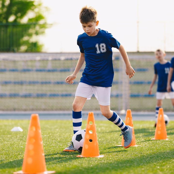 Fyra pojkar klädda i matchkläder dribblar fotbollar mellan orange konor på en gräsplan