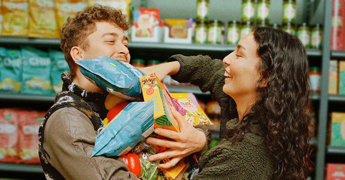 två glada personer håller upp varor i matbutik